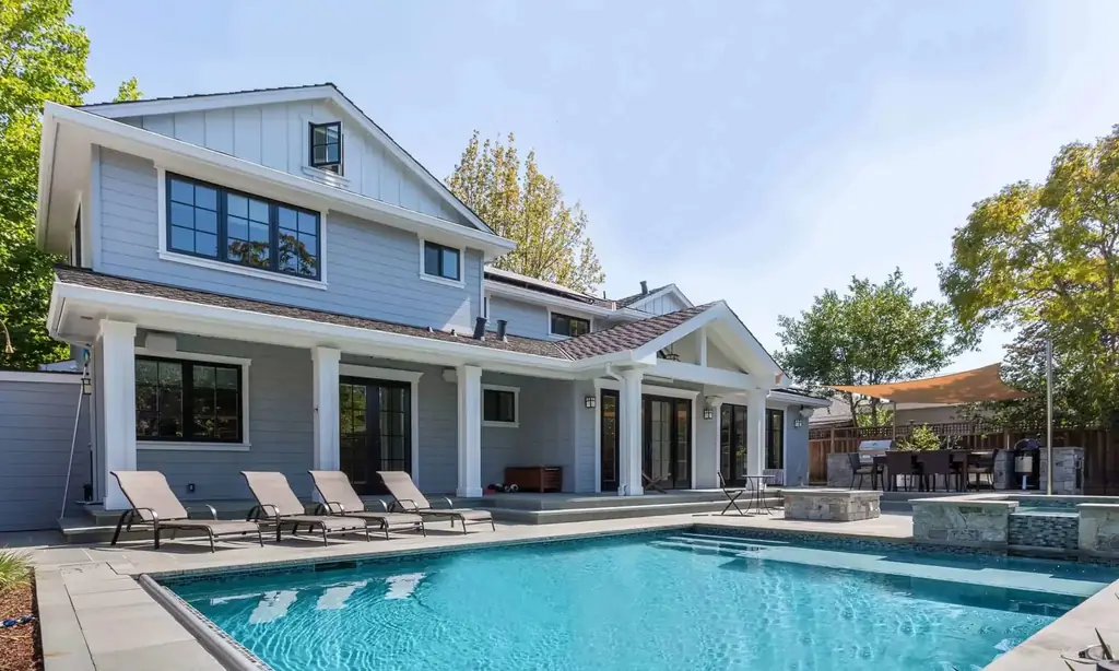 A grey board-and-batten home with a pool and loungers in the afternoon sun
